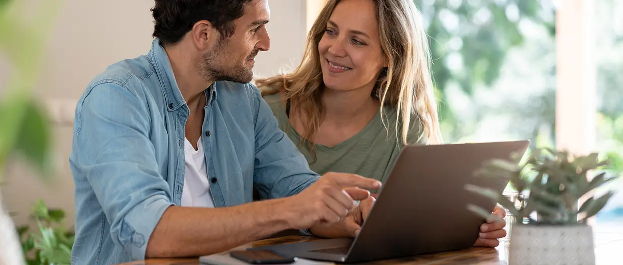 giovane coppia seduta davanti ad un laptop aperto si guarda negli occhi sorridendo