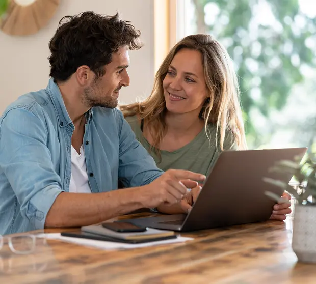 giovane coppia seduta davanti ad un laptop aperto si guarda negli occhi sorridendo