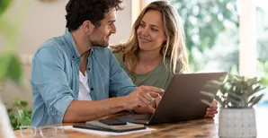 giovane coppia seduta davanti ad un laptop aperto si guarda negli occhi sorridendo