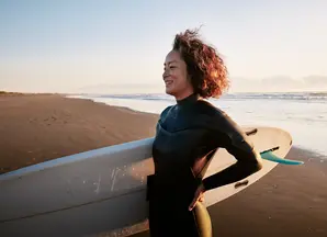 ragazza sorridente sulla spiaggia che imbraccia tavola da surf