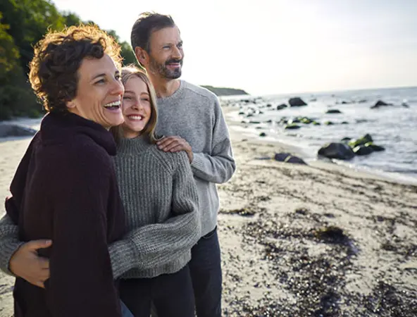 famiglia di tre persone in riva al mare sorridenti 