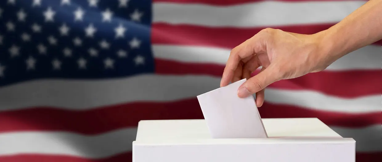 Hand hält Wahlzettel, die US-Flagge im Hintergrund