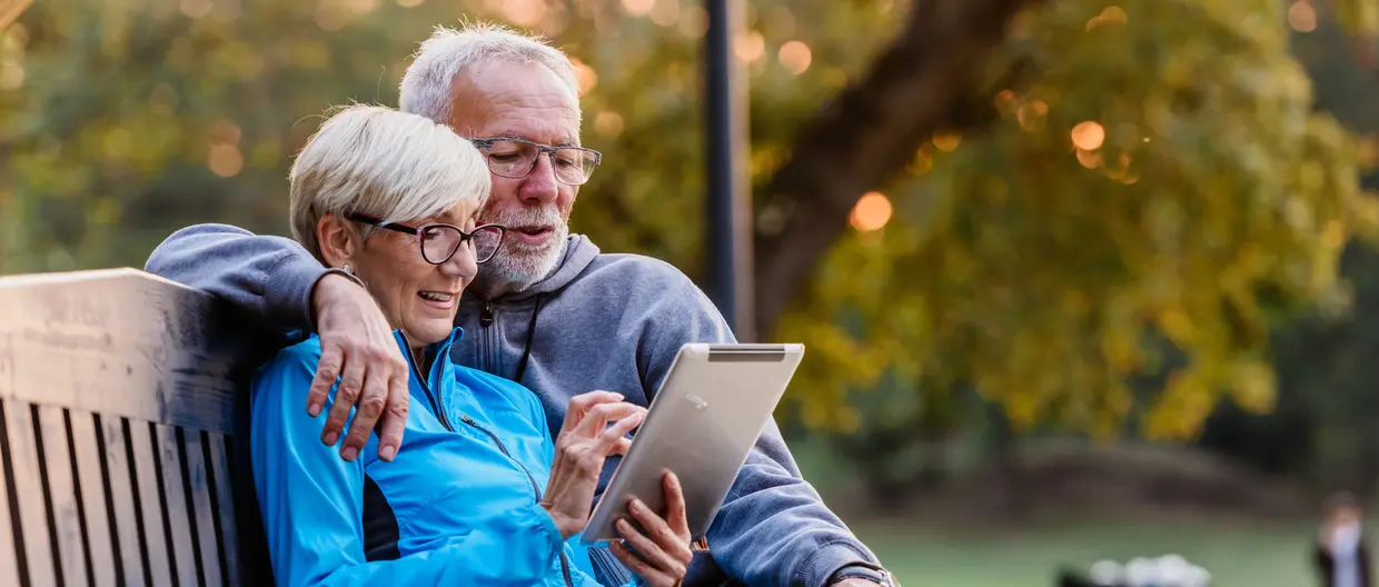 old couple on a bench looking at their tablet