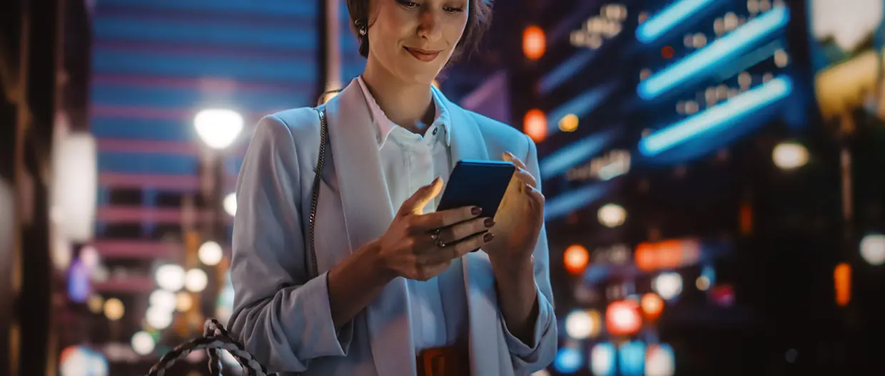 Ragazza che cammina tra i palazzi illuminati guardando il telefono