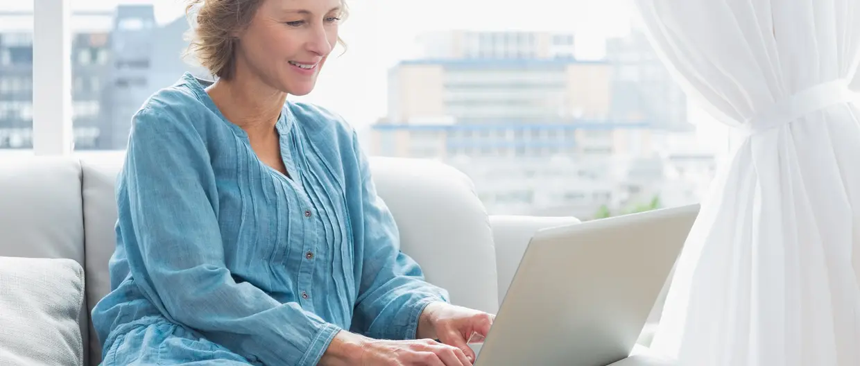 femme blonde assise sur son canapé tapotant sur son ordinateur portable 