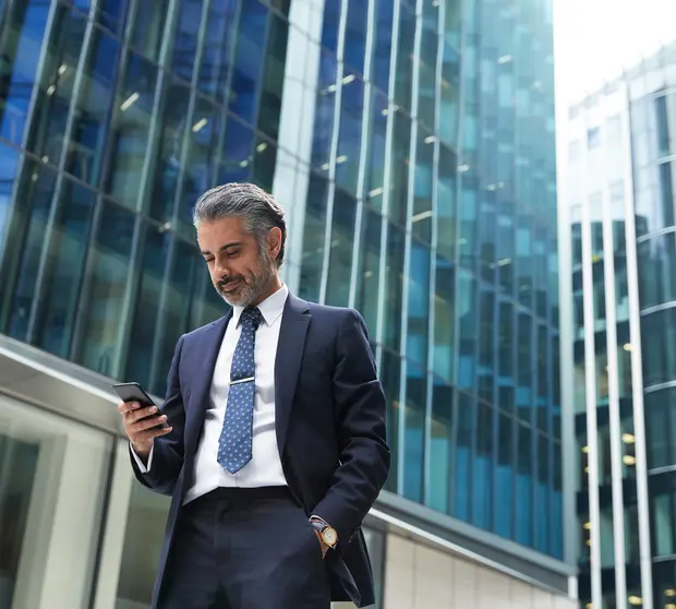 A business man is looking at his phone against tall office buildings.
