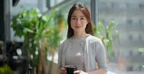Woman holding cup in office with potted plants behind
