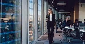 Woman looking out of an office window; colleagues in the background