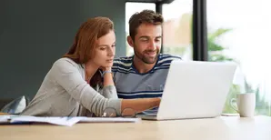 Couple sitting at a table looking at a laptop