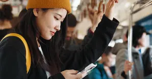A young woman is looking at her phone while commuting.