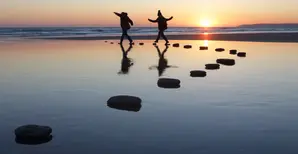 zwei Personen, die bei Sonnenuntergang auf Steinen über Wasser spazieren