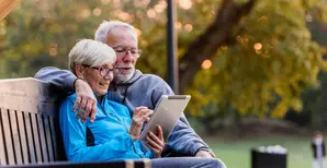 old couple on a bench looking at their tablet