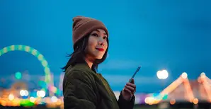 Sorridente giovane donna che utilizza uno smartphone in luna park
