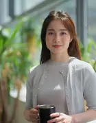 Woman holding cup in office with potted plants behind