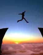 Person leaping over chasm at sunset