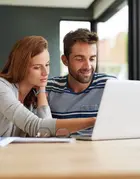 Couple sitting at a table looking at a laptop