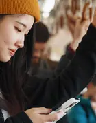 A young woman is looking at her phone while commuting.