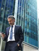 A business man is looking at his phone against tall office buildings.