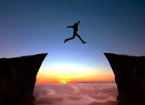 Person leaping over chasm at sunset