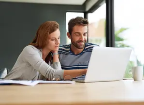Couple sitting at a table looking at a laptop
