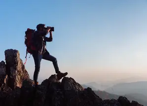 Mann mit Fernrohr auf einem Berggipfel 