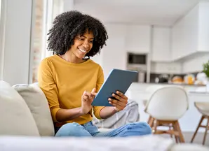 woman with a yellow jumper on her coach looking at her tablet