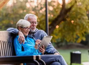 old couple on a bench looking at their tablet