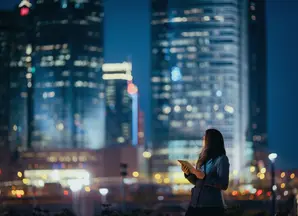 Young businesswoman using digital tablet, looking back over illuminated city skyline with confidence at night