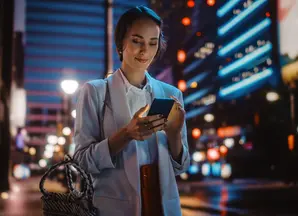 Ragazza che cammina tra i palazzi illuminati guardando il telefono