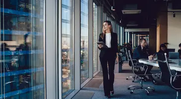 Woman looking out of an office window; colleagues in the background