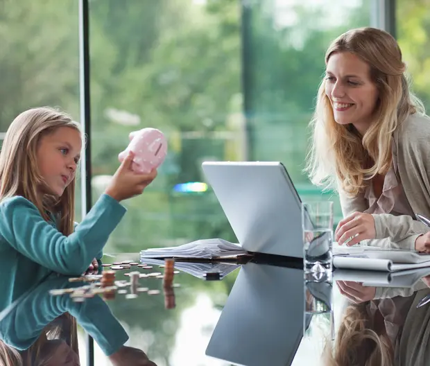 Mother and daughter sitting at table, counting coins from a piggy bank