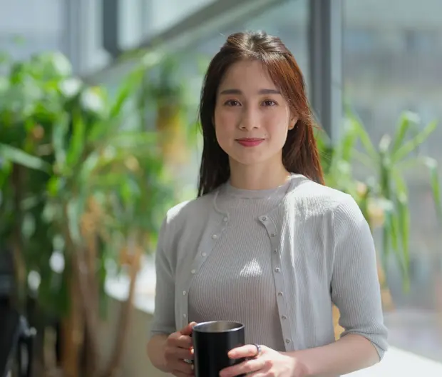 Woman holding cup in office with potted plants behind
