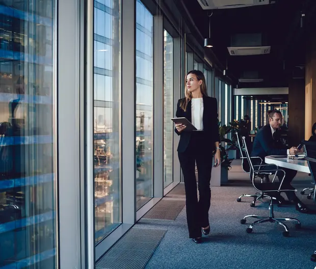 Woman looking out of an office window; colleagues in the background