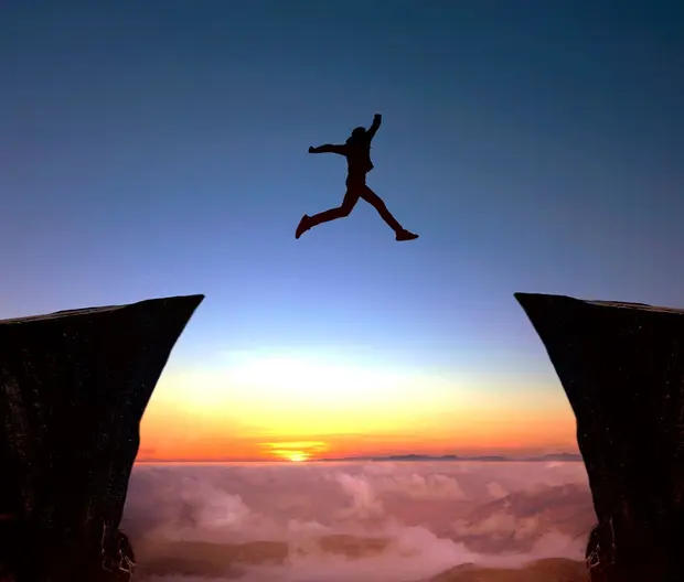 Person leaping over chasm at sunset