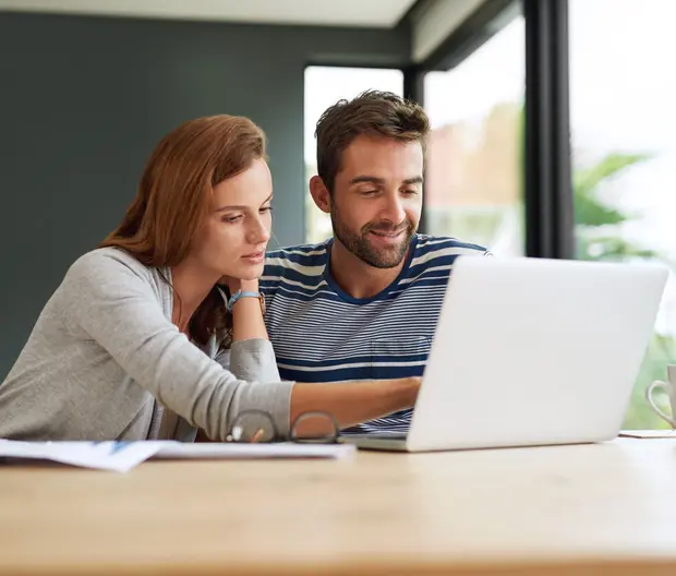 Couple sitting at a table looking at a laptop