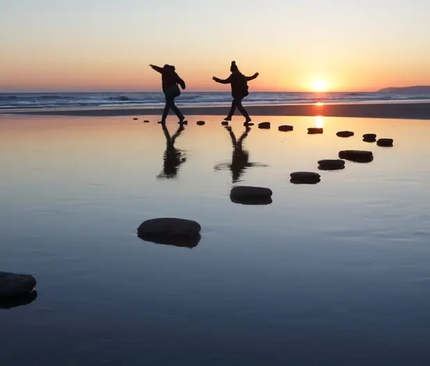 zwei Personen, die bei Sonnenuntergang auf Steinen über Wasser spazieren