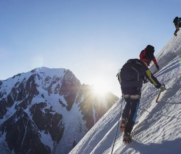 Un homme escalade une montagne enneigée avec deux autres