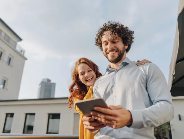 Two people smiling in front of building with tablet