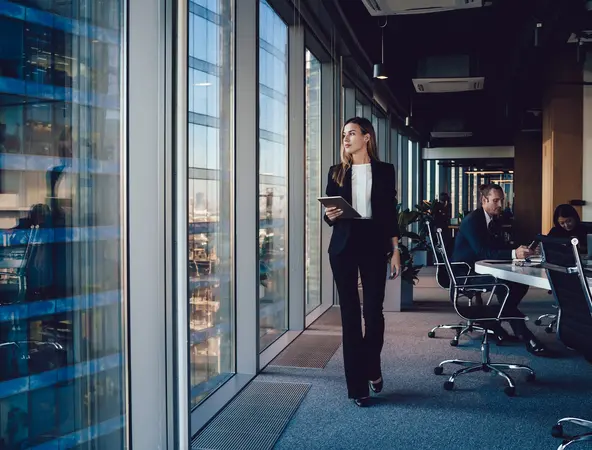 Woman looking out of an office window; colleagues in the background