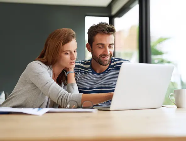 Couple sitting at a table looking at a laptop