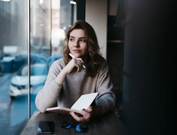 Pensive woman thinking with notebook at table