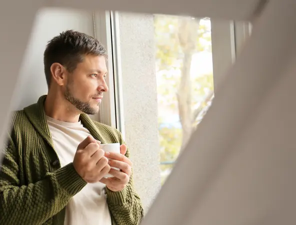 man drinking a cup of coffee and looking at the window