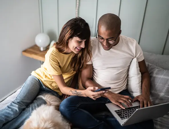 Frau und Mann mit Laptop und Handy lachend am Bett
