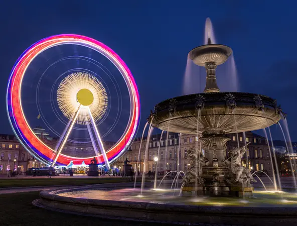 foto notturna di una ruota panoramica in movimento vicino ad una fontana pubblica