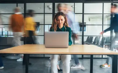 A focused asset manager works on a laptop in the Amundi offices as colleagues walk by.