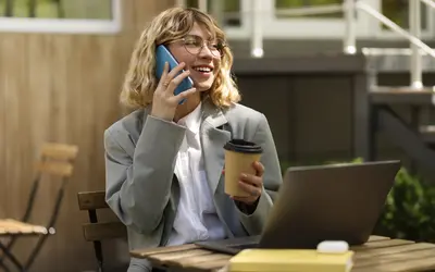 Asset manager on the phone, using a laptop with a coffee cup, working outdoors.