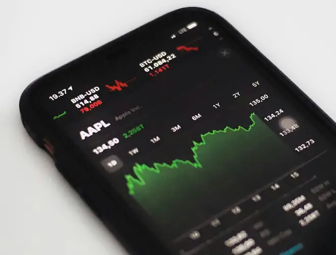 A smartphone displaying financial market data with a green line graph trend.