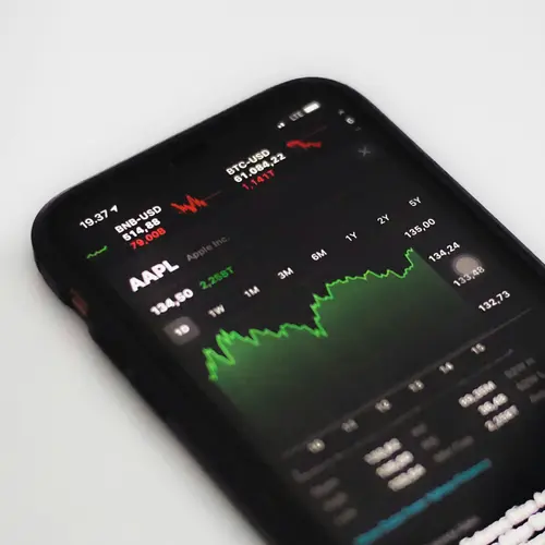 A smartphone displaying financial market data with a green line graph trend.