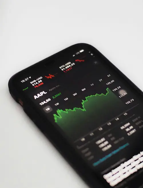 A smartphone displaying financial market data with a green line graph trend.