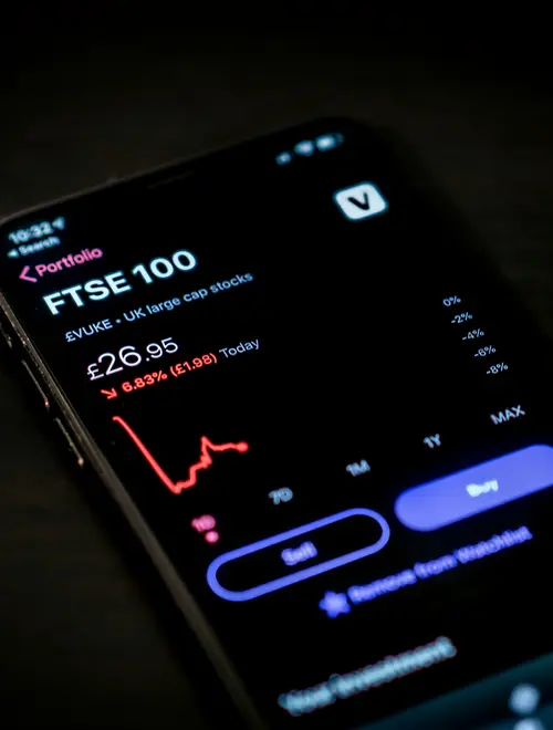 A smartphone displaying the FTSE 100 financial chart with a declining trend.